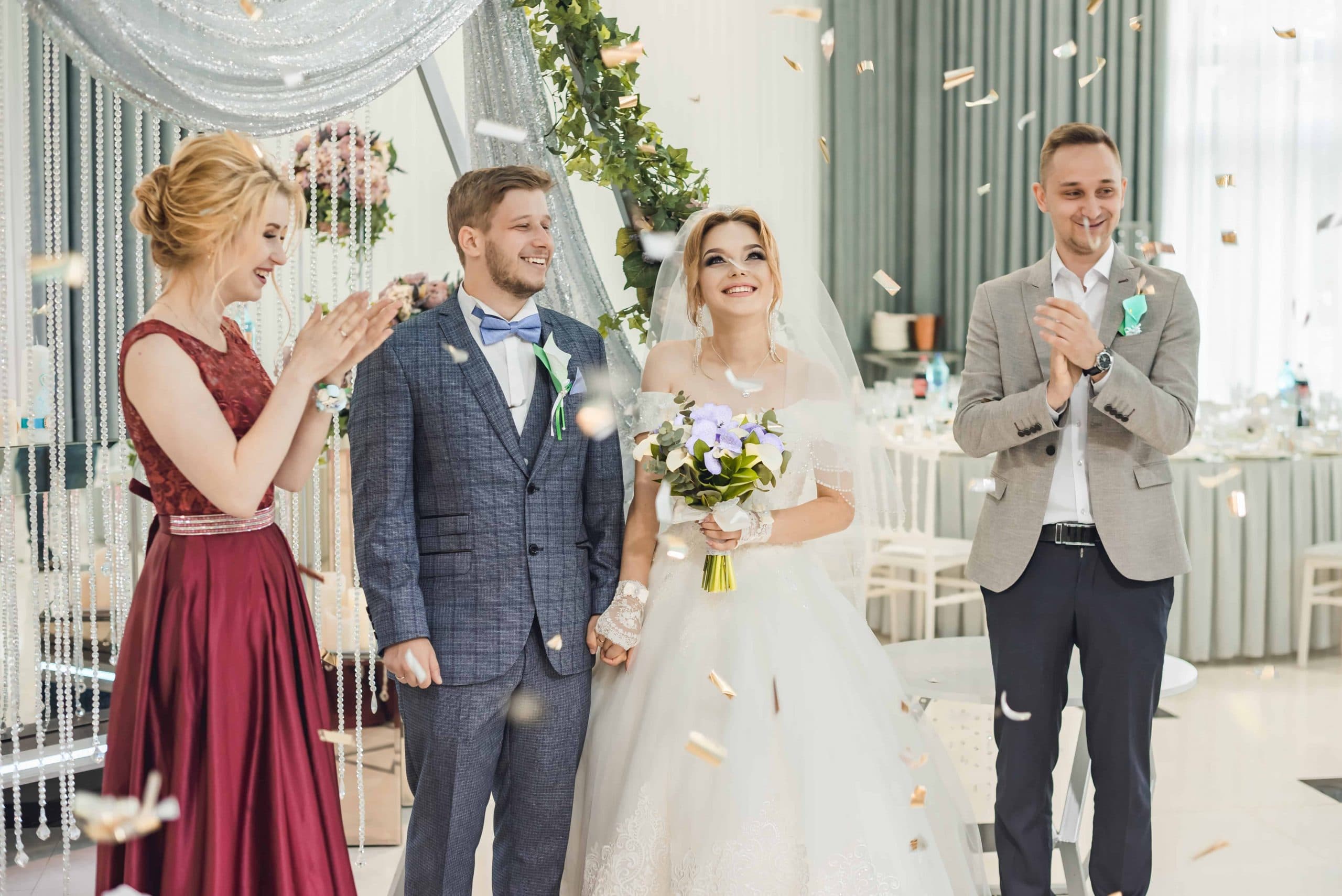 Dima and Alina Groisman stand in their wedding suit and dress as confetti falls around them and their family applauds.