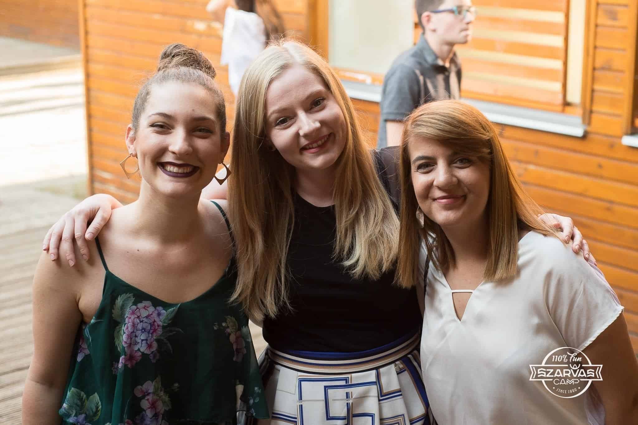 Rebeka Mucheva (right) stands outside a cabin with two friends and Camp Szarvas